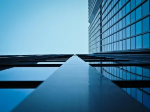Low-angle view of a modern blue glass building facade reflecting the sky, showing clean lines and rectangular patterns.
