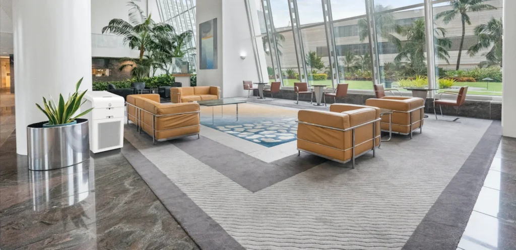 Spacious lobby with tan leather chairs, large windows, potted plants, and a white air purifier next to a large column.